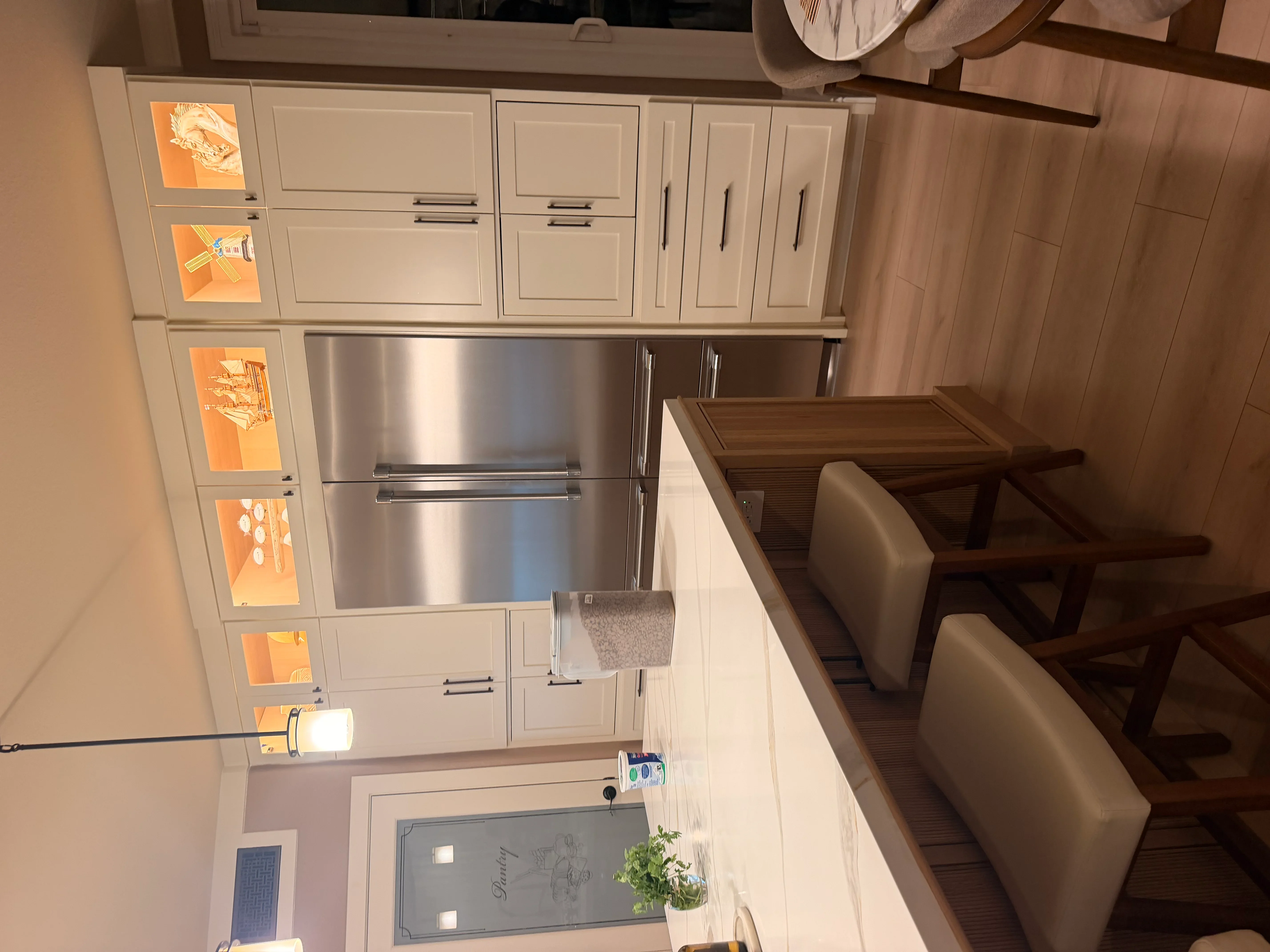 White cabinetry kitchen with stainless steel refrigerator, custom wood dining table, and recessed lighting